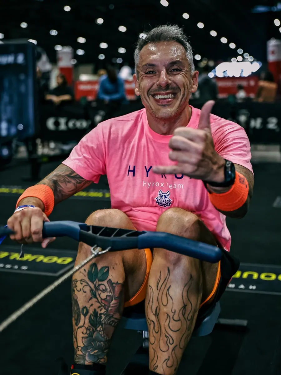 Atleta de camiseta rosa fazendo sinal de positivo no remo do HYROX, foto de PH Marx