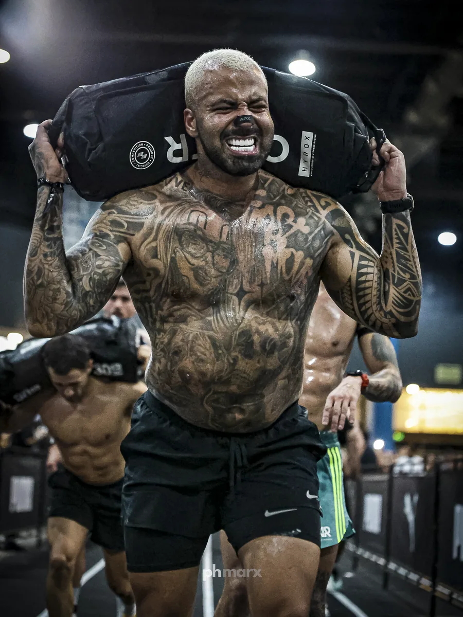 PH Marx fotografando atleta híbrido carregando sandbag no HYROX em São Paulo