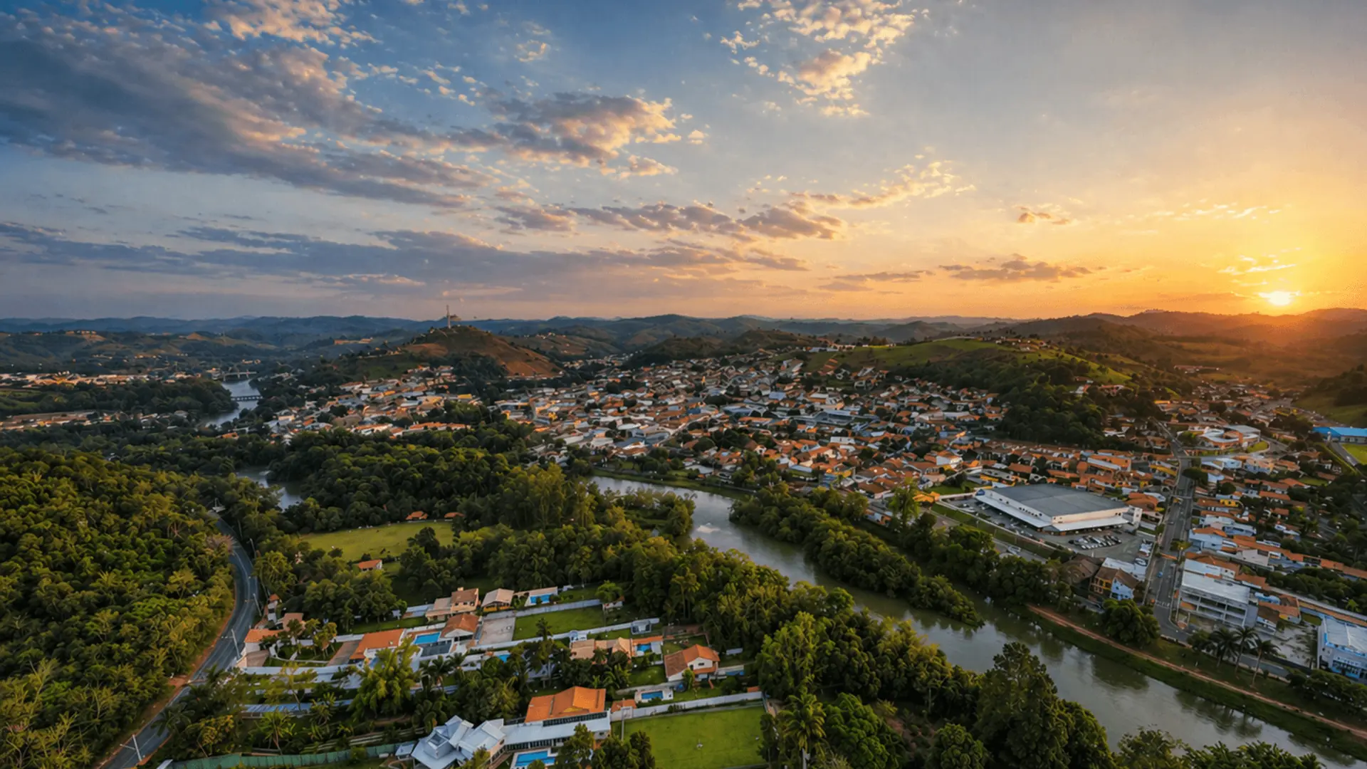 Vista aérea de drone ao entardecer de bairro residencial com casas, rio e colinas no interior de São Paulo