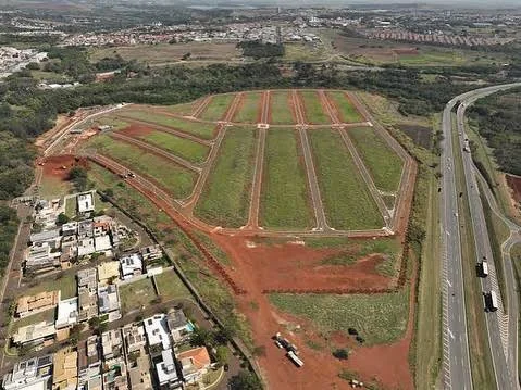 Vista aérea de loteamento com lotes demarcados e terraplenagem ao lado de rodovia
