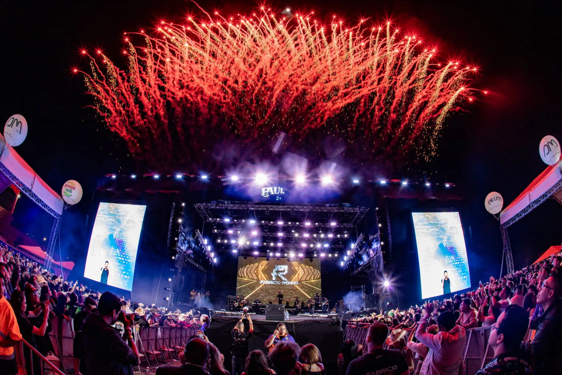 Show ao vivo à noite com chuva de fogos sobre o palco e público na grade, por PH Marx