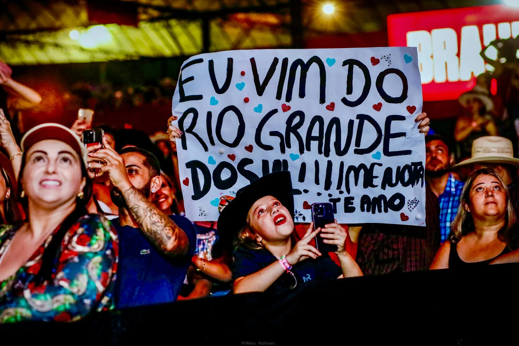 Cantora com chapéu e violão em close durante apresentação ao vivo