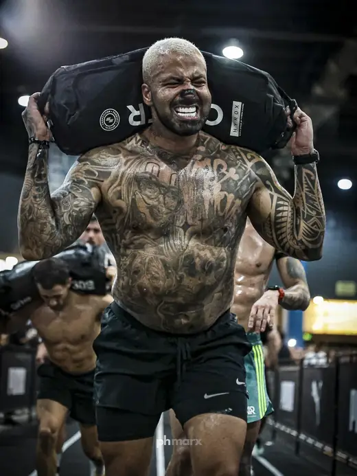Atleta tatuado carregando sandbag no HYROX São Paulo, por PH Marx