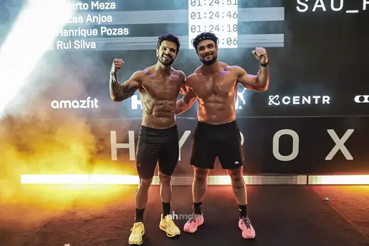Dois atletas comemorando na chegada do HYROX com fogo no palco, por PH Marx