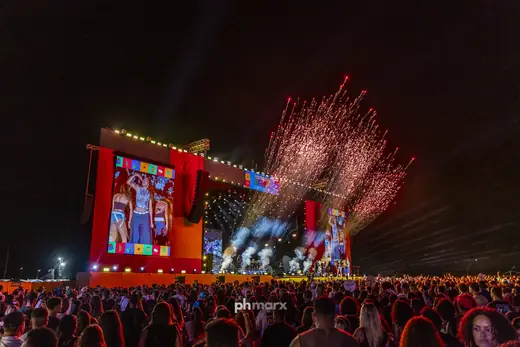 Palco de festival com fogos e plateia lotada à noite, por PH Marx
