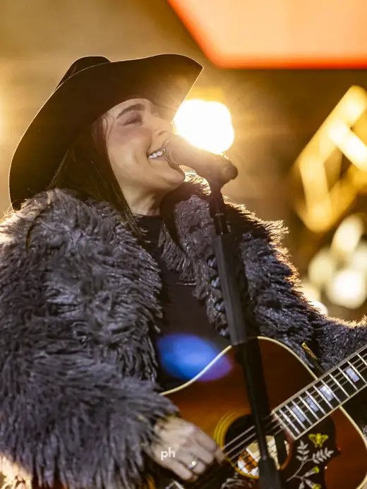 Cantora de chapéu com violão em close durante show ao vivo, por PH Marx